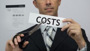 Male office worker or businessman in a suit and tie cuts a piece of paper with the word costs on it as a cost reduction business concept.