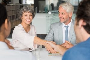 Close up of a cheerful senior business woman shaking hands with businessman. Business people shaking hands in meeting. Handshake between mature leadership and young business man.